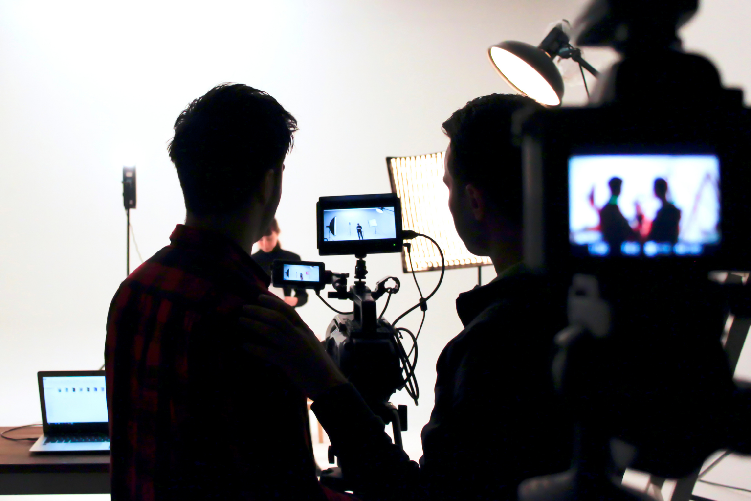 Two crew members working behind cameras in a bright professional television or video production studio