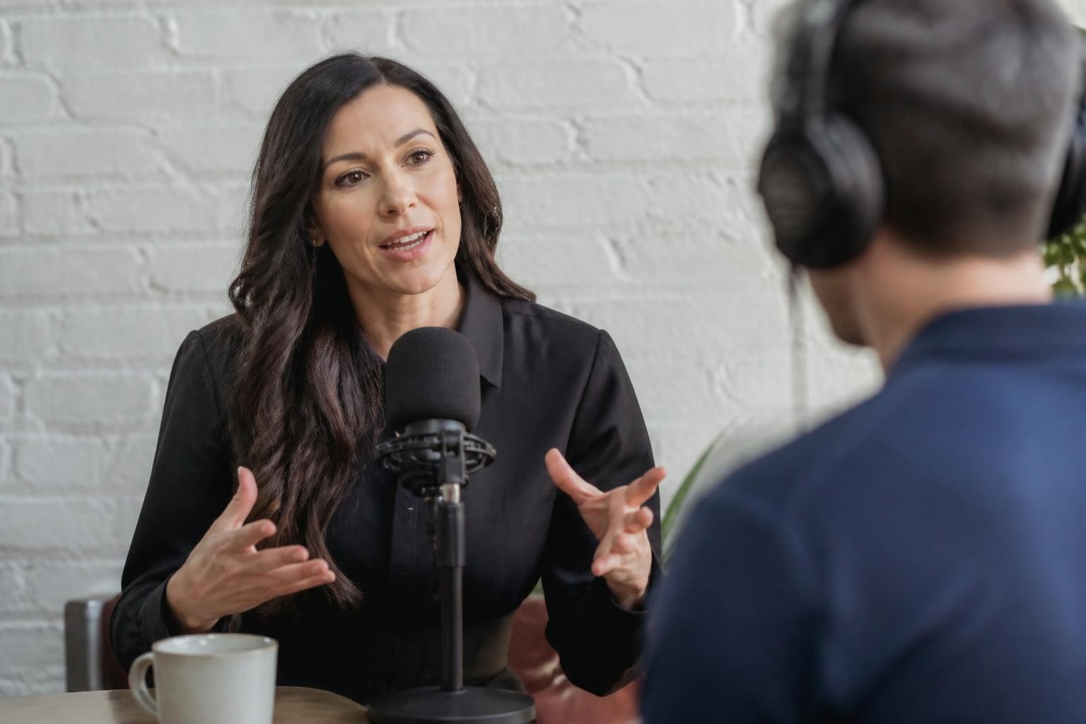 Professional woman speaking into a podcast microphone while being interviewed in a studio setting.